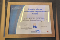 Framed certificate for the National Improvement Award recognising HPFT, displayed on a table.