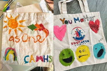 Two hand-painted tote bags displayed side by side. The left bag features a large orange sun, a rainbow, kites and the words "as one" and "CAMHS" in colourful letters. The right bag shows the text 'You Matter' with two large hearts, the Educatch Charity logo, and three emoticons: smiling, neutral, and sleeping.