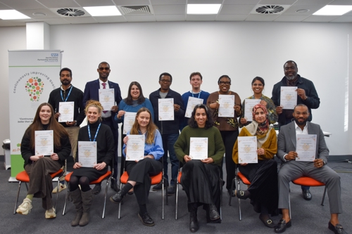 Group photo of people seated and standing in a meeting room, each holding a certificate.