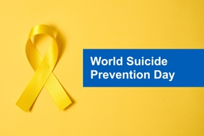 Yellow ribbon on a yellow background with white writing on a blue background saying World Suicide Prevention Day